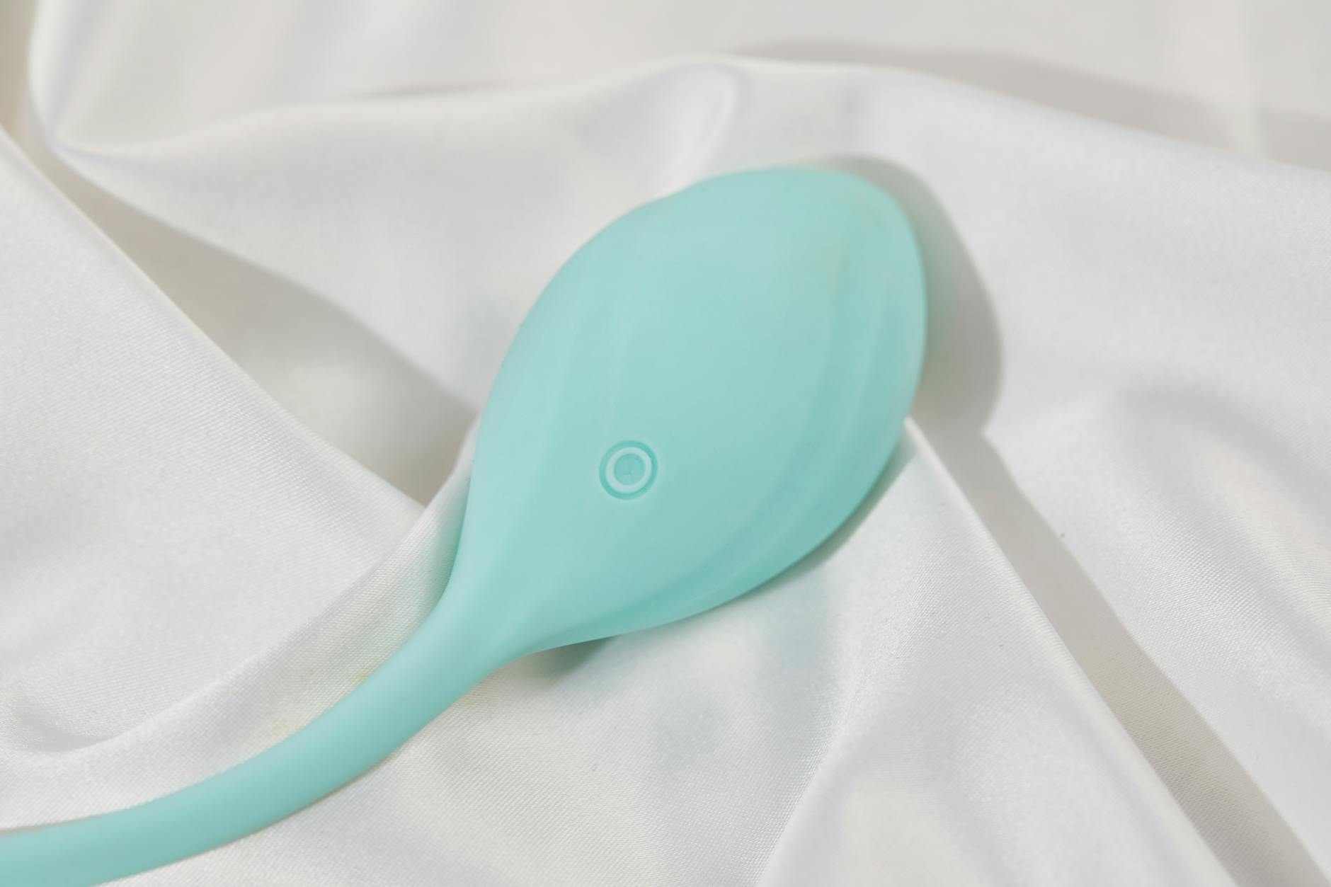 Un vibrador teal moderno sobre tela de seda blanca, perfecto para la intimidad solitaria