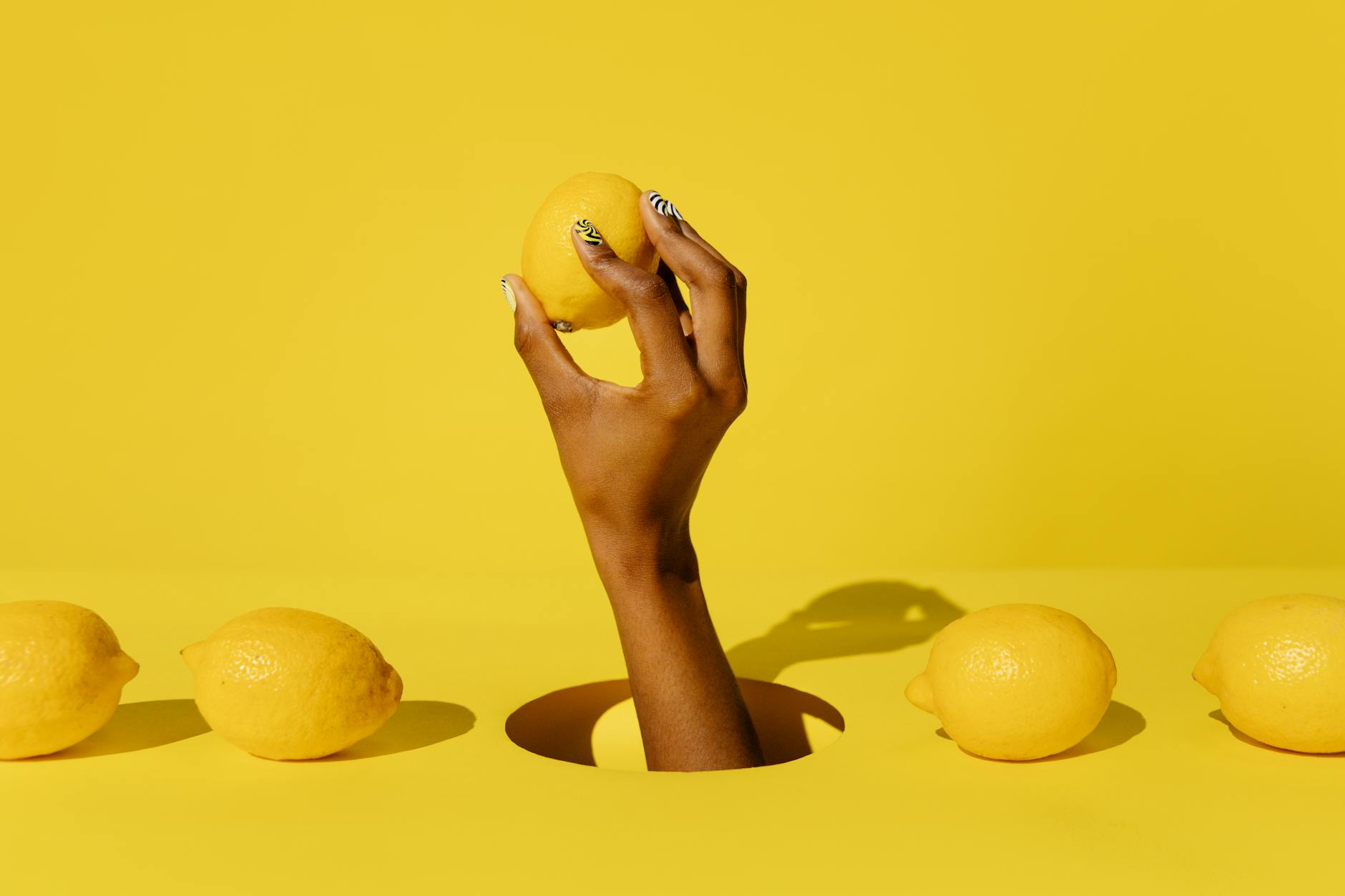 A hand holding a fresh lemon against a vivid yellow background, symbolizing renewal and fresh starts