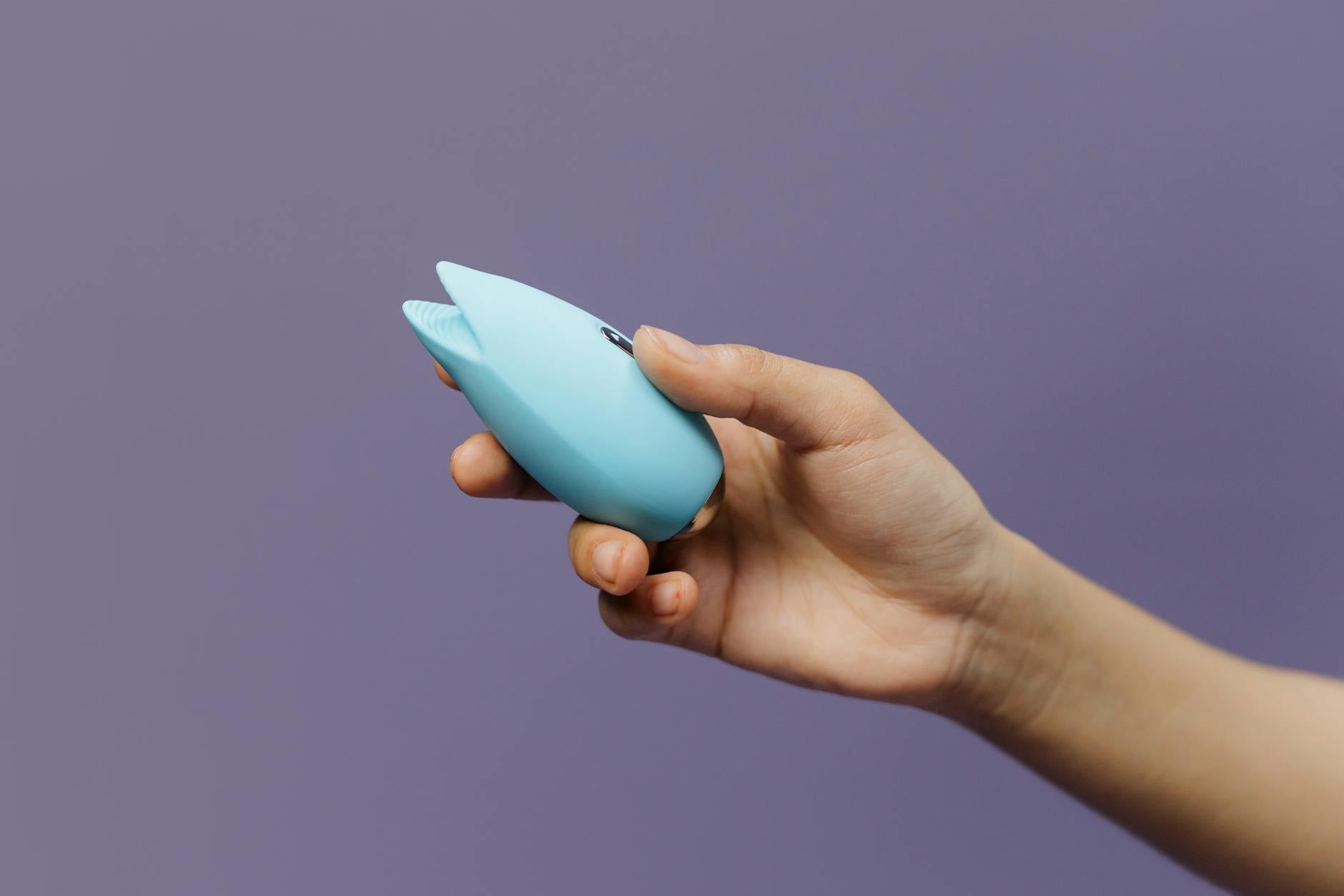 A blue clitoral vibrator in hand against a purple background