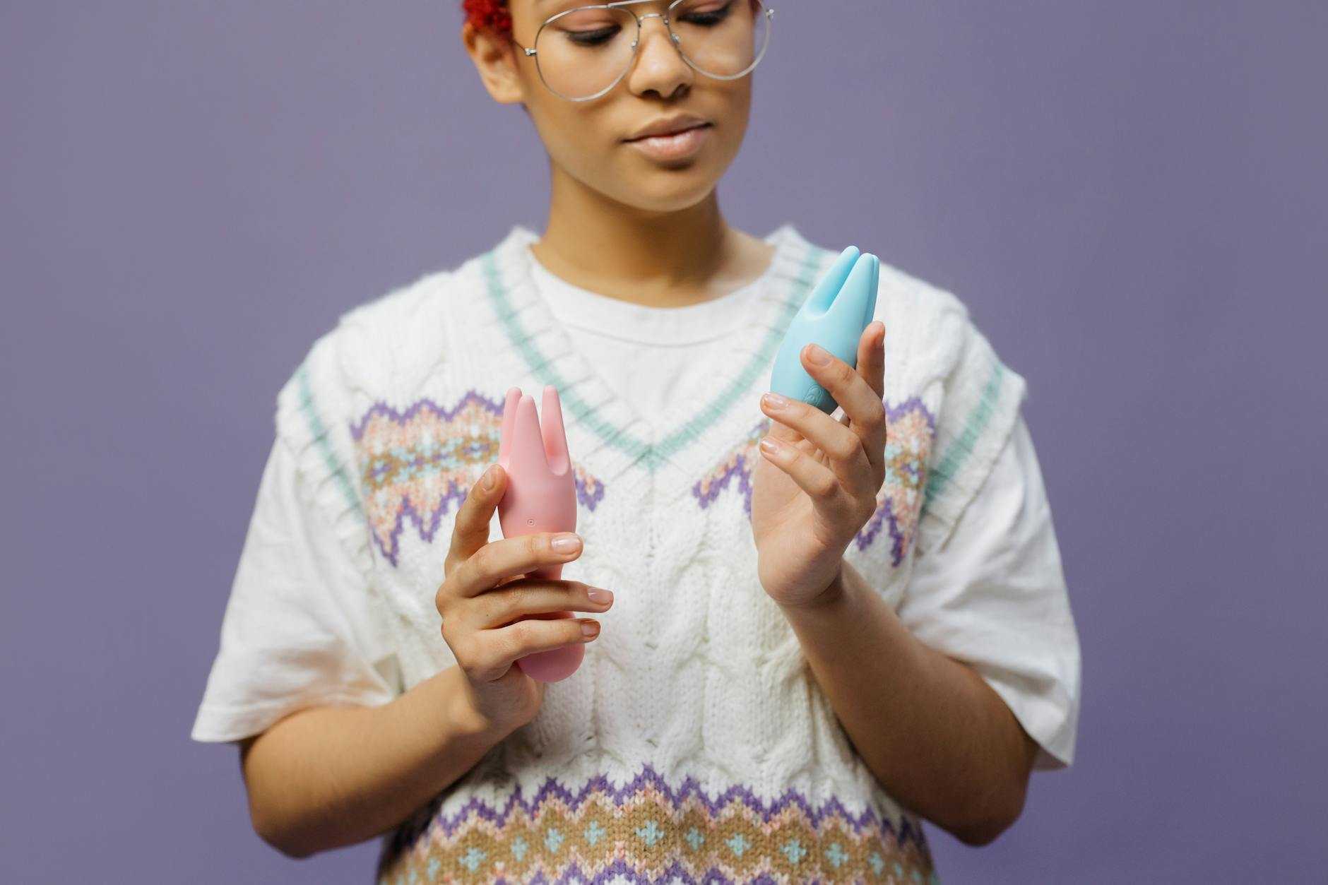 Woman contemplating blue and pink silicone vibrators, representing thoughtful pleasure exploration