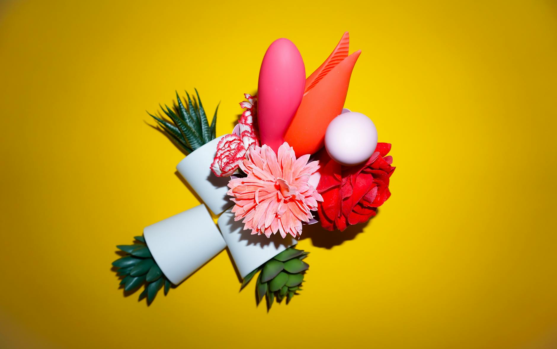 A blue vibrator surrounded by fresh flowers and orange slices on a yellow background